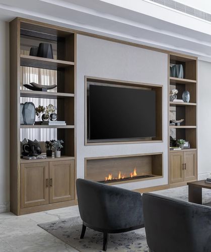 Living room with wood shelving unit, mounted TV, linear fireplace and two grey velvet armchairs