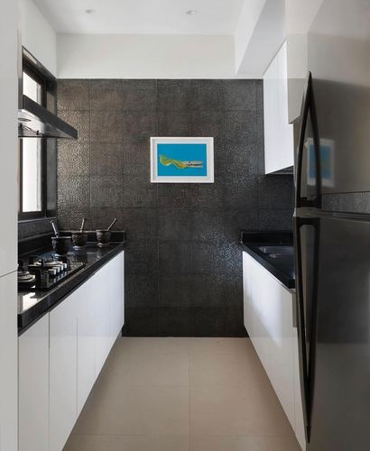 Narrow galley kitchen with black textured tile wall, white glossy cabinets, and steel fridge