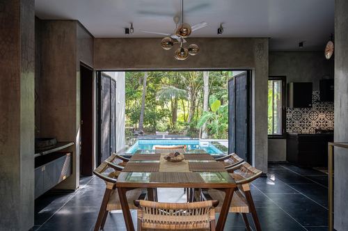 Dining table with cane chairs facing open doors to pool and greenery