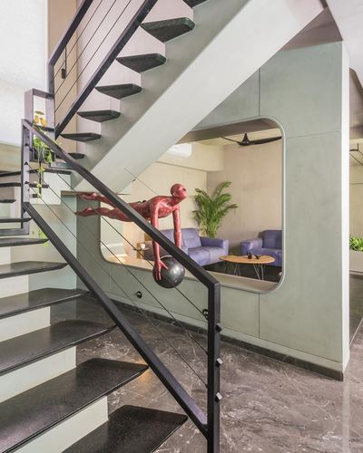 Staircase with black metal railing and red figurative sculpture beside a rounded cutout opening into a living room.