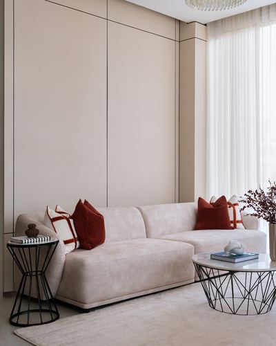 Beige living room with paneled wall, neutral sectional sofa, rust pillows, and wire coffee tables.
