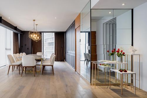 Long dining room with marble table beneath geometric chandelier beside a mirrored wall corridor