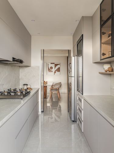 Galley kitchen in soft greige tones with stone counters, glass cabinet, and view through to dining area