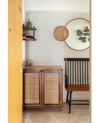 Entryway with wooden door numbered 1302, cane-front cabinet, round mirror and spindle bench