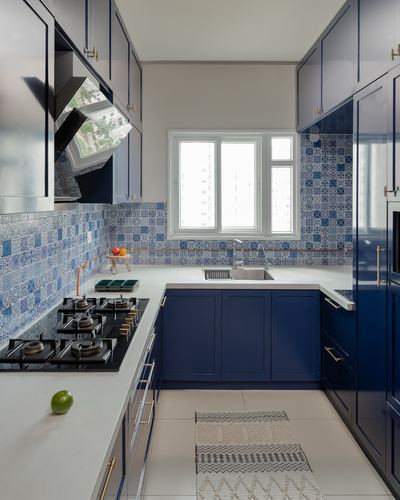 Navy blue modular kitchen with patchwork blue tile backsplash and white countertops