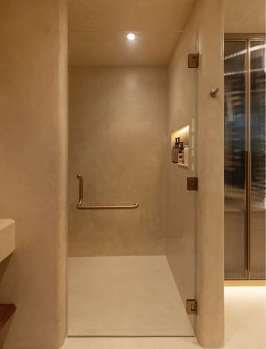 Curved plaster walk-in shower with glass door and brass grab bar in warm-toned bathroom
