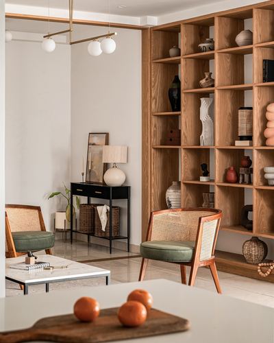 Living room with cane armchairs, marble table, and a tall wood display shelf styled with vases