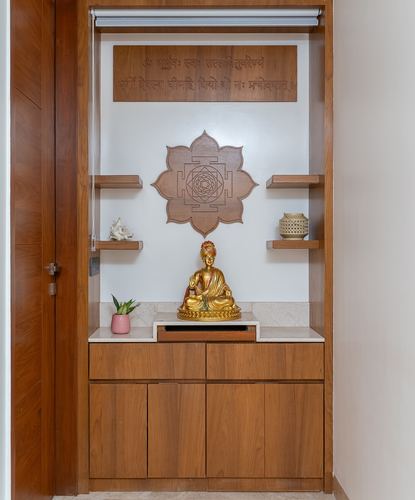 Wooden pooja niche with carved lotus panel, brass idol, and floating shelves
