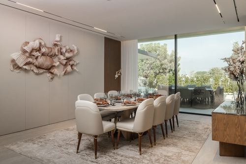 Elegant dining room with long table, upholstered chairs, sculptural wall art, and garden view