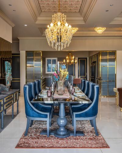 Long dining table with navy velvet chairs under a crystal chandelier in an ornate gold-trimmed room