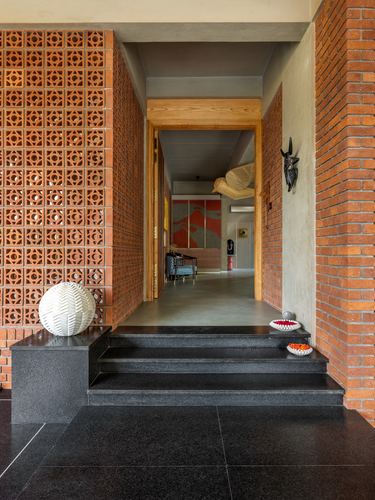 Entrance hallway with brick jaali walls, black granite steps, and a distant timber-framed doorway