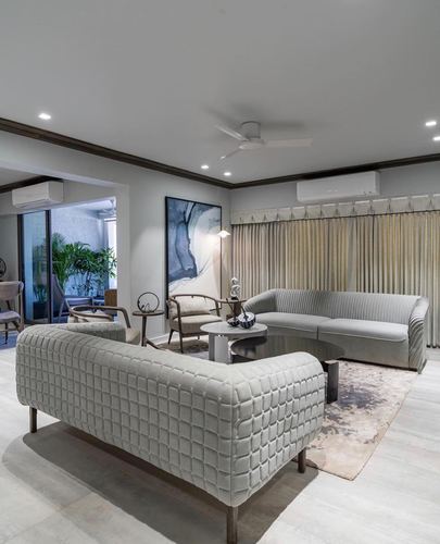 Grey living room with curved sofa, quilted bench, round tables, abstract art and sheer curtains
