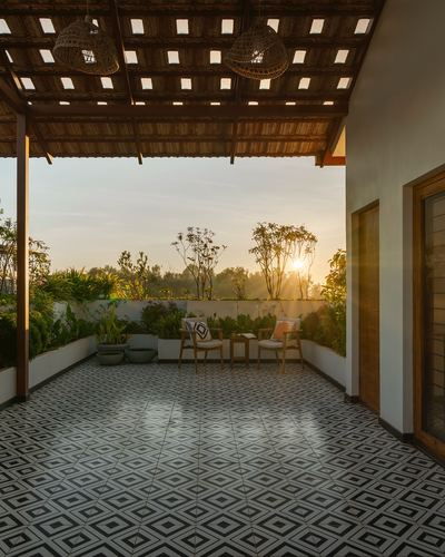 Covered veranda with patterned tile floor, rattan pendant lights, and sunset view through trees