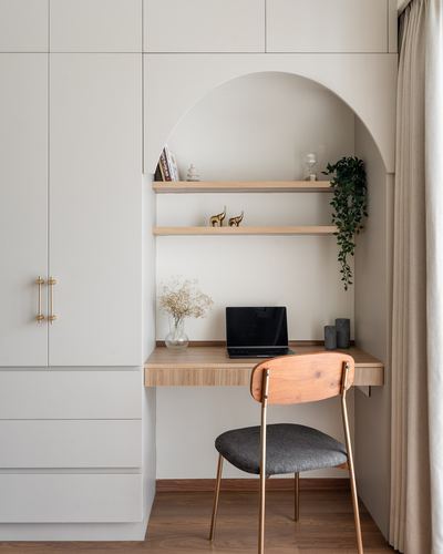 Arched nook with wooden desk, floating shelves, laptop, and a cane-back chair beside white wardrobes