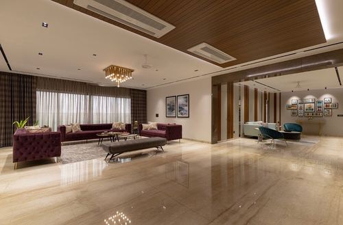 Spacious living room with merlot tufted sofas, wood-panelled ceiling, and reflective marble floor in Surat apartment