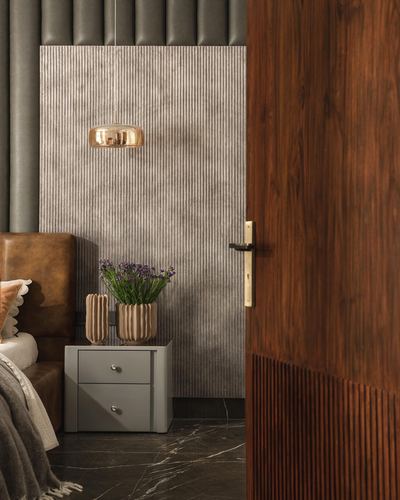 Bedroom corner with brass pendant light, fluted grey wall, leather headboard, and open ribbed wood door