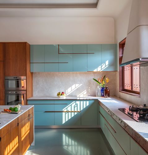 Teal and wood kitchen with stone countertops and morning sunlight through window grille