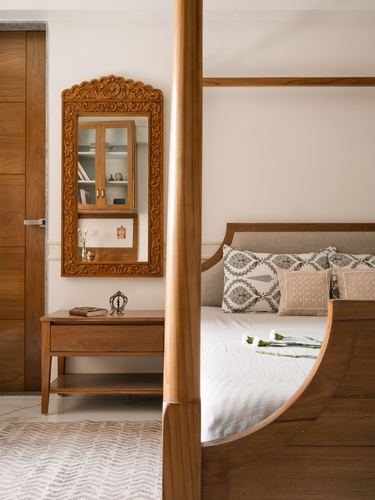 Bedroom with carved wooden mirror, four-poster teak bed, and patterned cushions