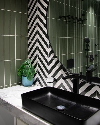 Bathroom vanity with black vessel sink, marble counter, chevron tile and curved mirror