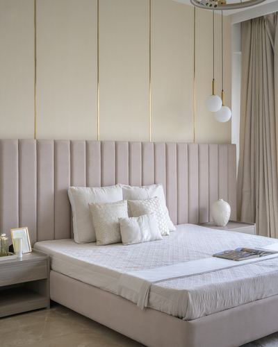 Blush channel-tufted bed against cream wall with brass inlay strips and globe pendant lights