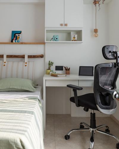 White study desk with office chair beside a bed with green striped linen