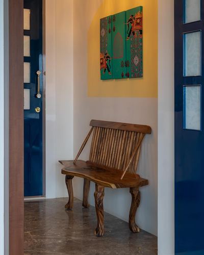 Wooden bench in a mustard-lit foyer niche below a green elephant motif triptych, beside a blue door