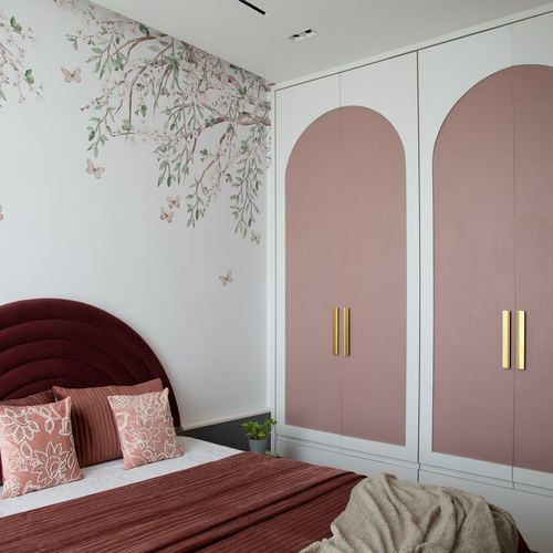 Pink arched wardrobe doors and maroon scalloped headboard beside a floral mural wall