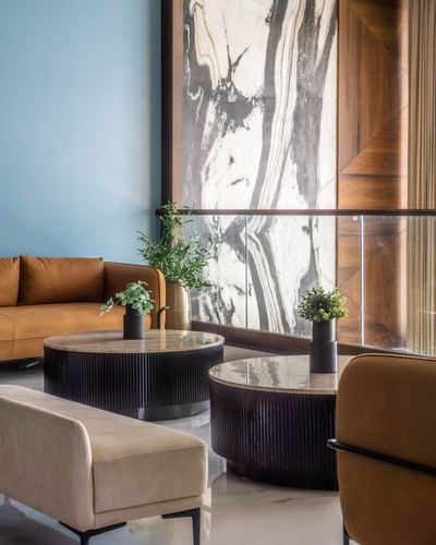 Living room corner with fluted round coffee tables, camel leather sofa, and marble-clad wall panel