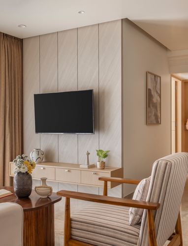 Beige fluted panel tv wall with floating console, striped armchair and wooden table in foreground