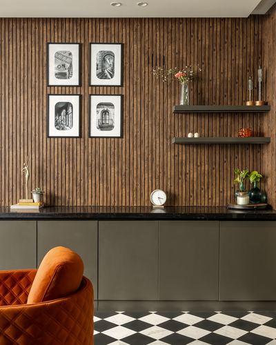 Wood-slatted wall with framed prints above a black-topped console and orange velvet chair