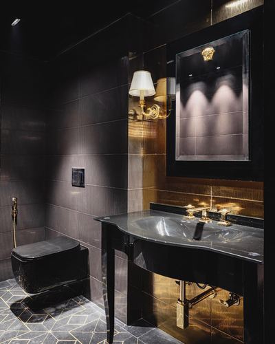 Dark luxury powder room with black marble sink, brass fittings, and mirror with gold medallion.
