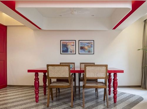 Red dining table with turned legs and cane chairs under a red-trimmed ceiling coffer