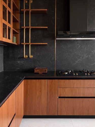 L-shaped kitchen with wood cabinetry, black stone walls, brass-suspended shelves, and gas hob