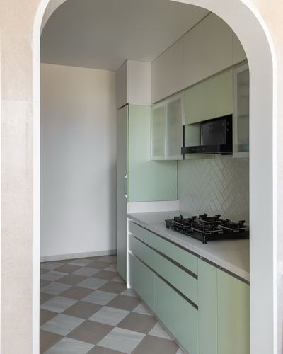 Arched doorway framing a sage-green galley kitchen with herringbone tile backsplash and checkerboard floor