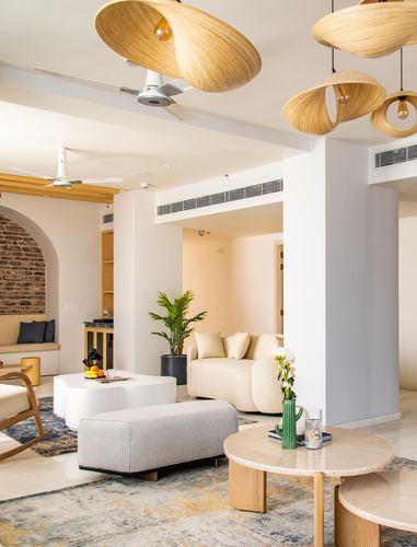Living room with curved cream furniture, marble tables, and sculptural rattan pendant lights under an arched brick niche