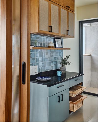 Kitchen corner with wood cane cabinets, patterned blue tile backsplash, black countertop and wicker basket drawers