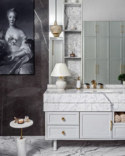 Marble bathroom vanity with brass fixtures beside a framed classical portrait on dark stone wall