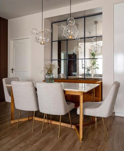 Dining table with marble top, grey chairs, brass legs, under bubble pendant lights facing mirror panel