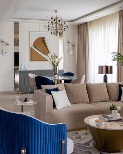 Beige and navy living room with brass chandelier, sectional sofa, and dining area beyond
