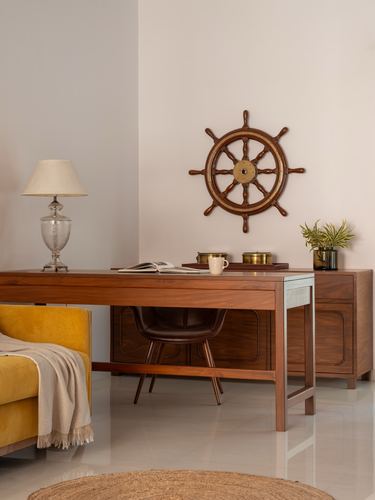 Wooden desk with leather chair, mustard sofa, and ship's wheel wall decor against white wall