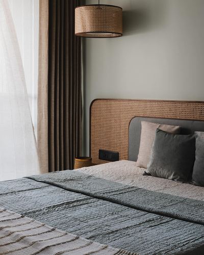 Bedroom corner with cane headboard, grey upholstered bed, sheer curtains and rattan pendant light