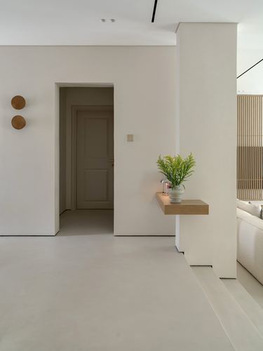 Minimalist beige foyer with floating wood shelf, vase, and view into living room through fluted screen