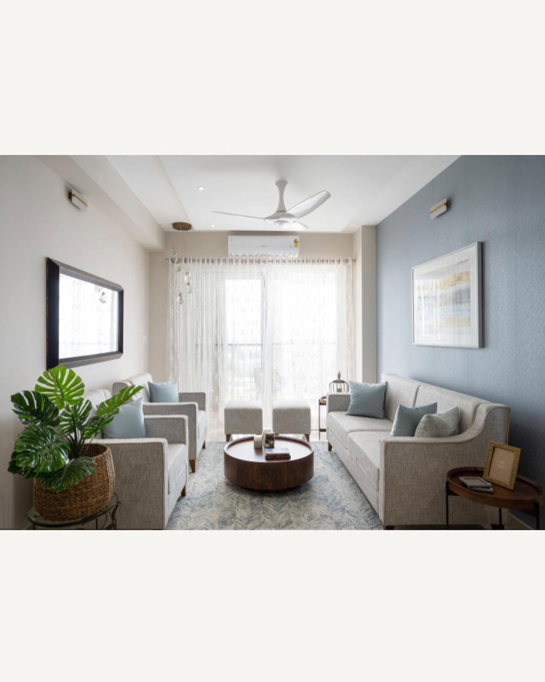 Grey sofa seating around a round wood table in a blue-accented living room with sheer curtains