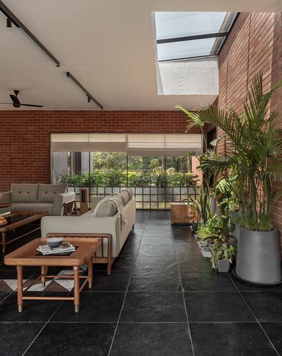 Living room with exposed brick walls, dark stone floor, skylight, and large potted plants