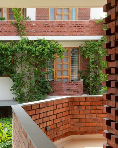 Brick jaali facade with curved balconies, timber window grilles, and climbing green vines in Jaipur homestay
