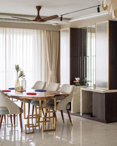 Dining room with live-edge wood table, brass geometric legs, upholstered chairs, and mirrored dark wood console.
