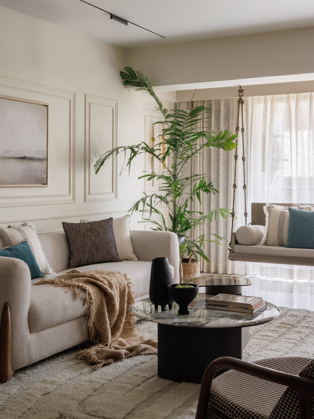 Neutral living room with panel moulding, beige sofa, round stone-top coffee table, and a hanging swing by the window