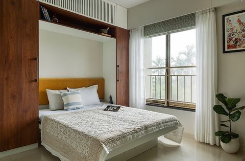 Bedroom with wood-framed bed niche, mustard headboard, sheer curtains and balcony view