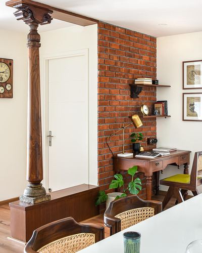 Carved wooden Chettinad pillar beside brick wall study nook with desk and cane chairs