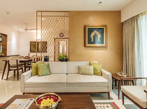 Living room with beige sofa, mustard textured wall, framed arch artwork, and gold metal jali screen dividing dining area